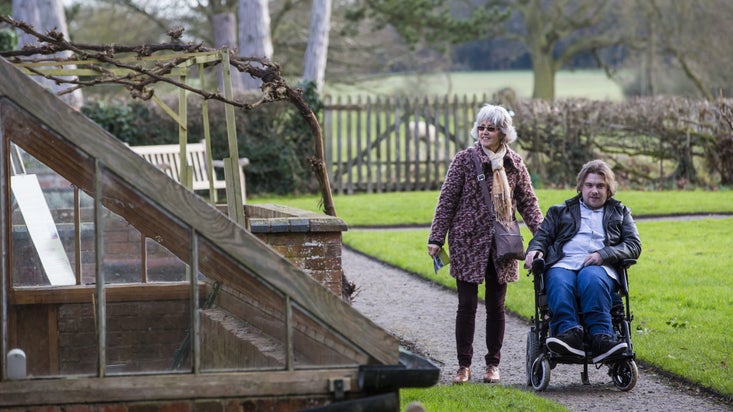 Visitor in wheelchair with woman walking alongside him exploring the garden in February at Baddesley Clinton, Warwickshire